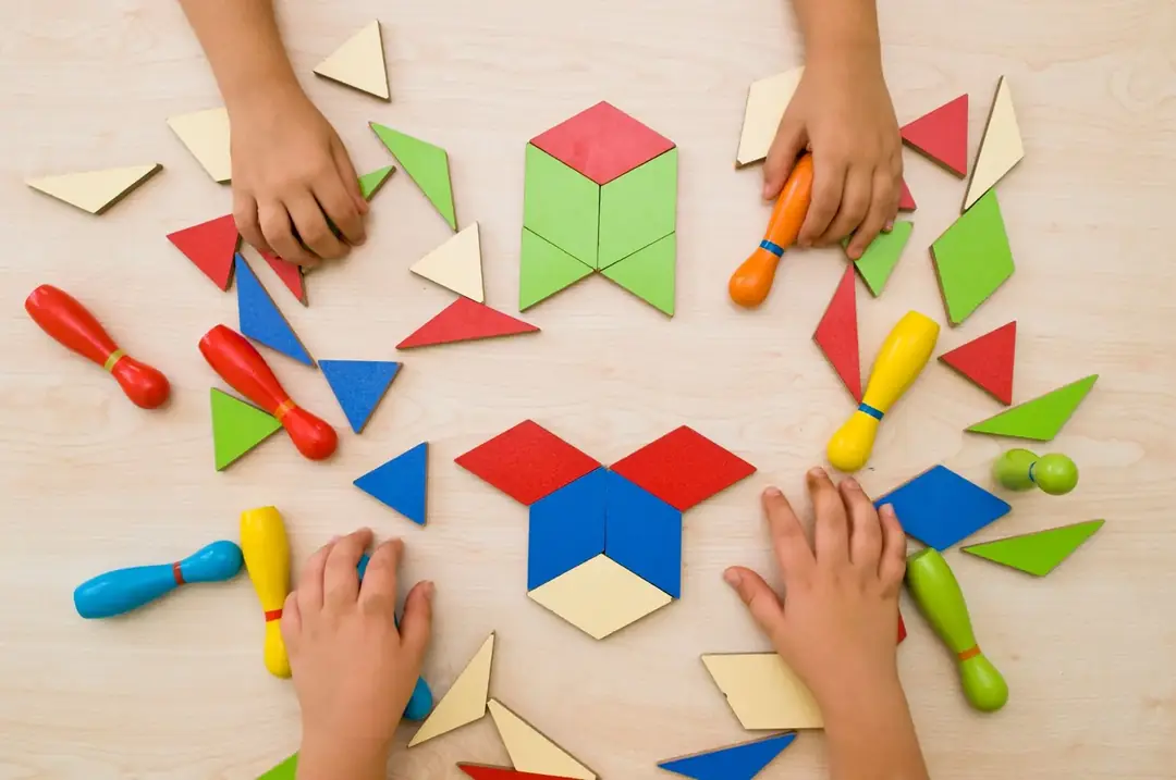 Children's hands arranging colourful Montessori geometric shapes and wooden pegs on a table